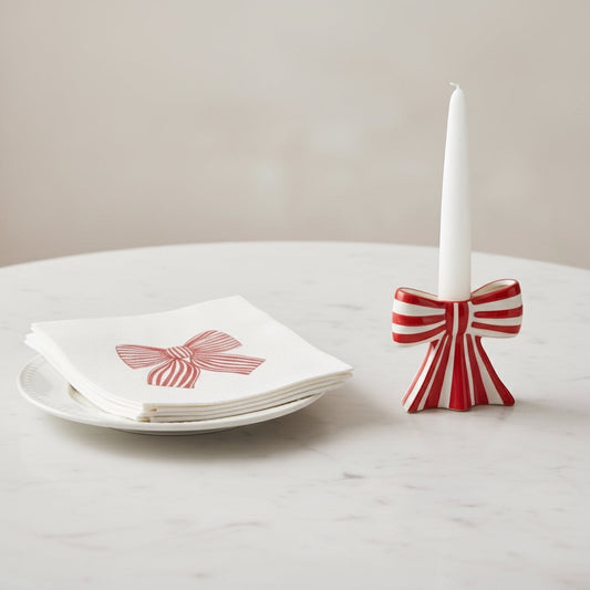 Eclectic red and white striped ceramic bow candle holder with a taper candle next to a matching napkin on a plate.