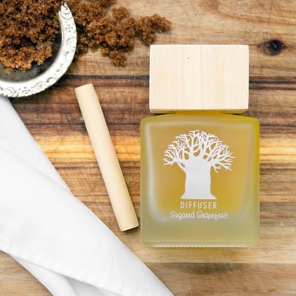 Eclectic Sugared Grapefruit diffuser in a frosted glass bottle with a natural wooden lid on a rustic wooden surface.