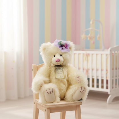 Eclectic Suki Lola Silver Tag Bear in white plush with a lilac tulle corsage, sitting on a wooden chair in a nursery.