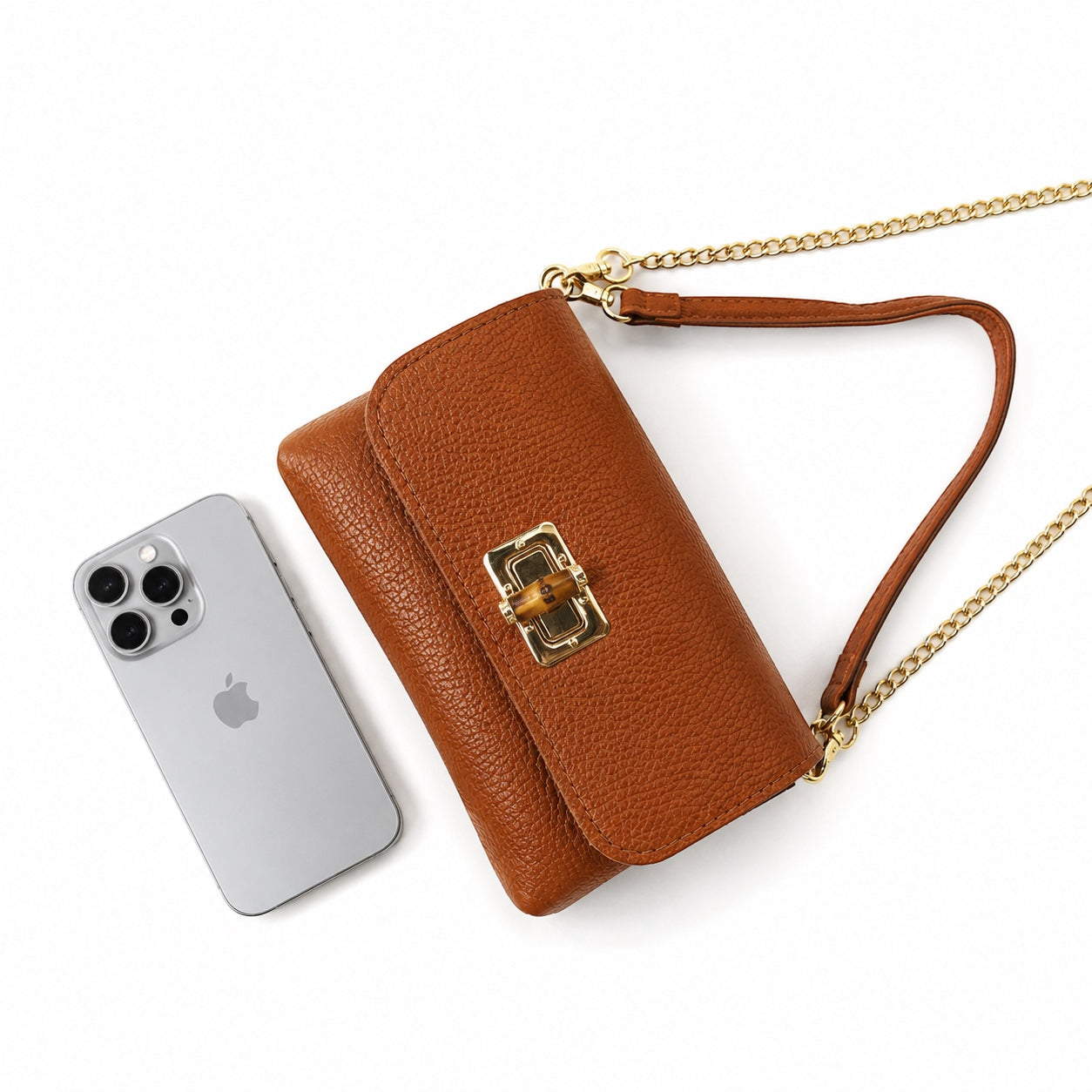 Eclectic tan pebbled leather clutch with gold chain strap and bamboo-style clasp next to a smartphone