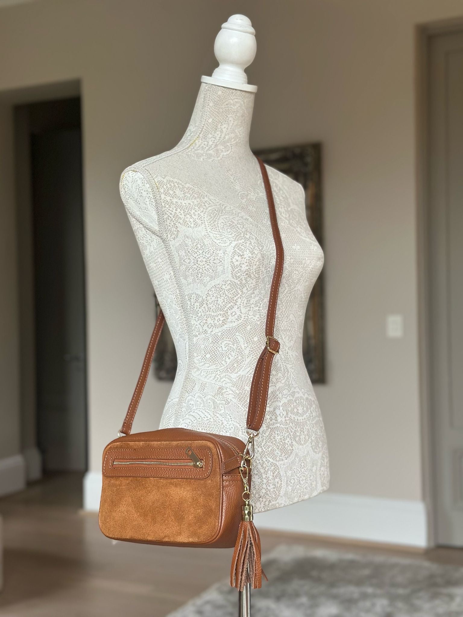 Eclectic tan suede and leather crossover bag with double tassels and adjustable strap on a mannequin