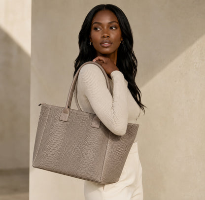 Model carrying a taupe snake-print suede shopper bag from Eclectic, featuring top handles and a structured design.
