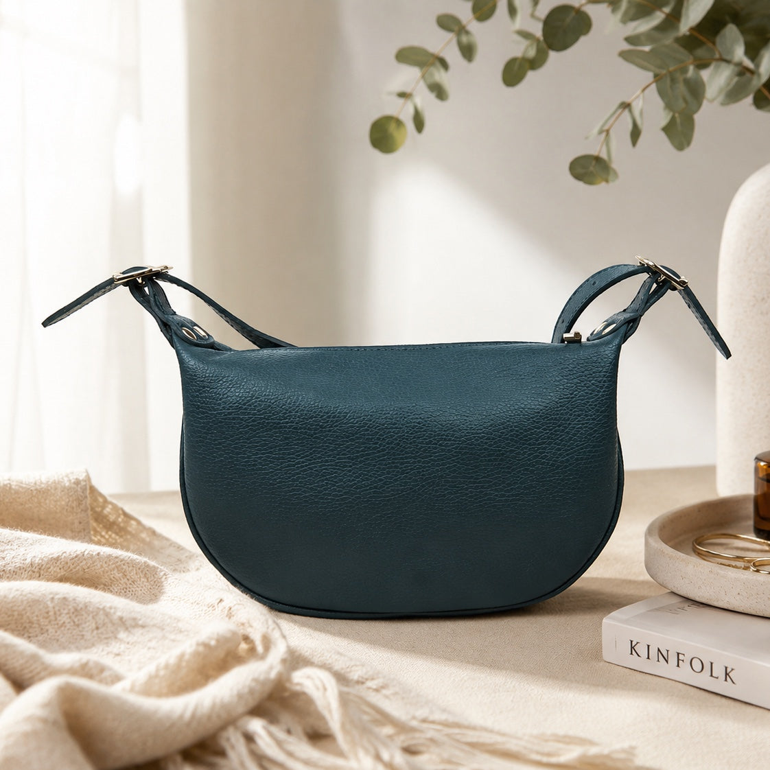 Eclectic dark teal grained leather half moon sling bag with a crescent silhouette and adjustable strap.
