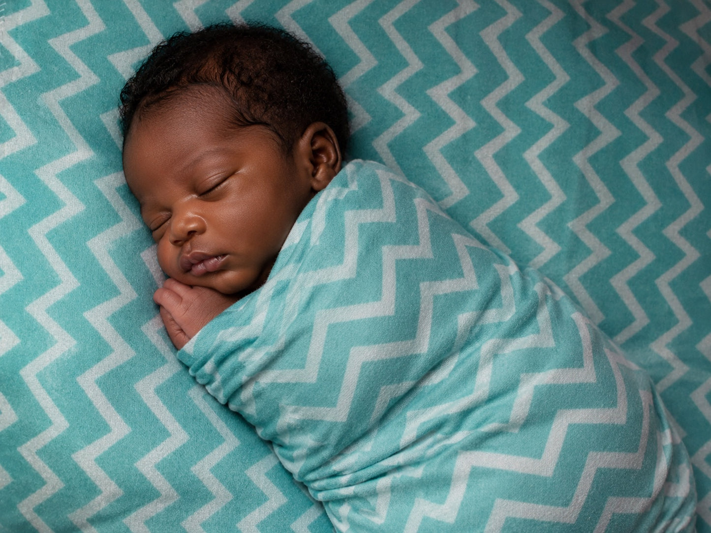 Eclectic baby swaddled in a soft turquoise and white chevron cotton flannel blanket sleeping peacefully