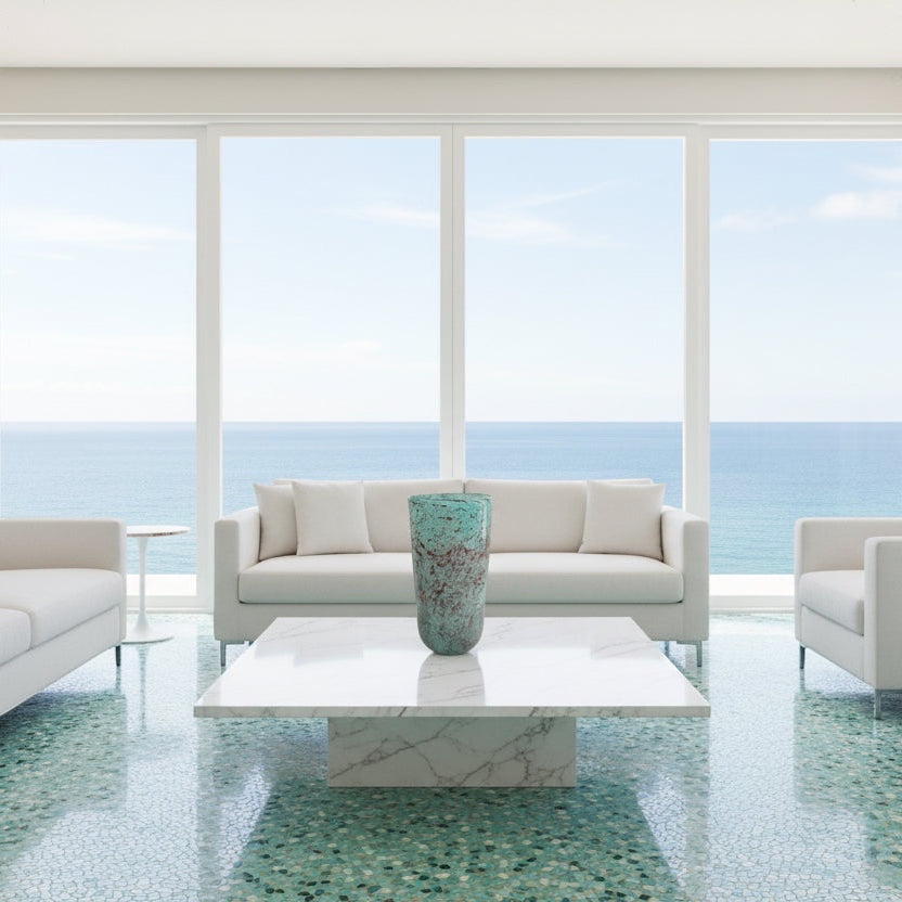 Eclectic textured turquoise glass cylinder vase displayed on a white marble coffee table in a coastal living room.