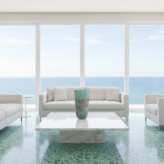 Eclectic textured turquoise glass cylinder vase displayed on a white marble coffee table in a coastal living room.