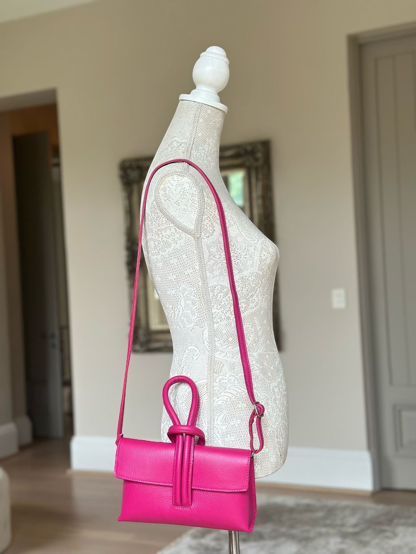 Eclectic Venezia hot pink pebbled leather crossbody bag with a unique looped handle on a mannequin display.