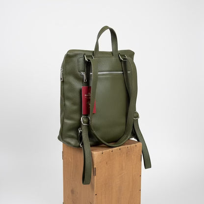 Eclectic Verona olive green pebbled leather backpack with adjustable straps and back zip pocket on a wooden block.