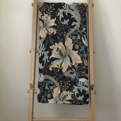 Eclectic vintage floral round tablecloth in black, cream, green, and gold drip dry fabric draped on a wooden ladder.