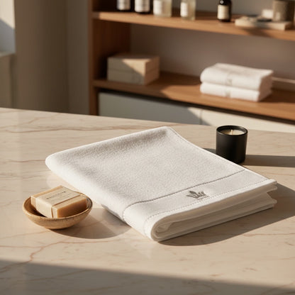 Eclectic white cotton guest towel with embroidered crown detail folded on a marble countertop with soap and candle.