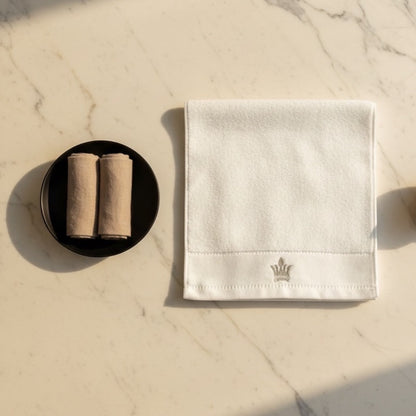Eclectic white cotton guest towel with an elegant embroidered crown detail, displayed on a marble surface.