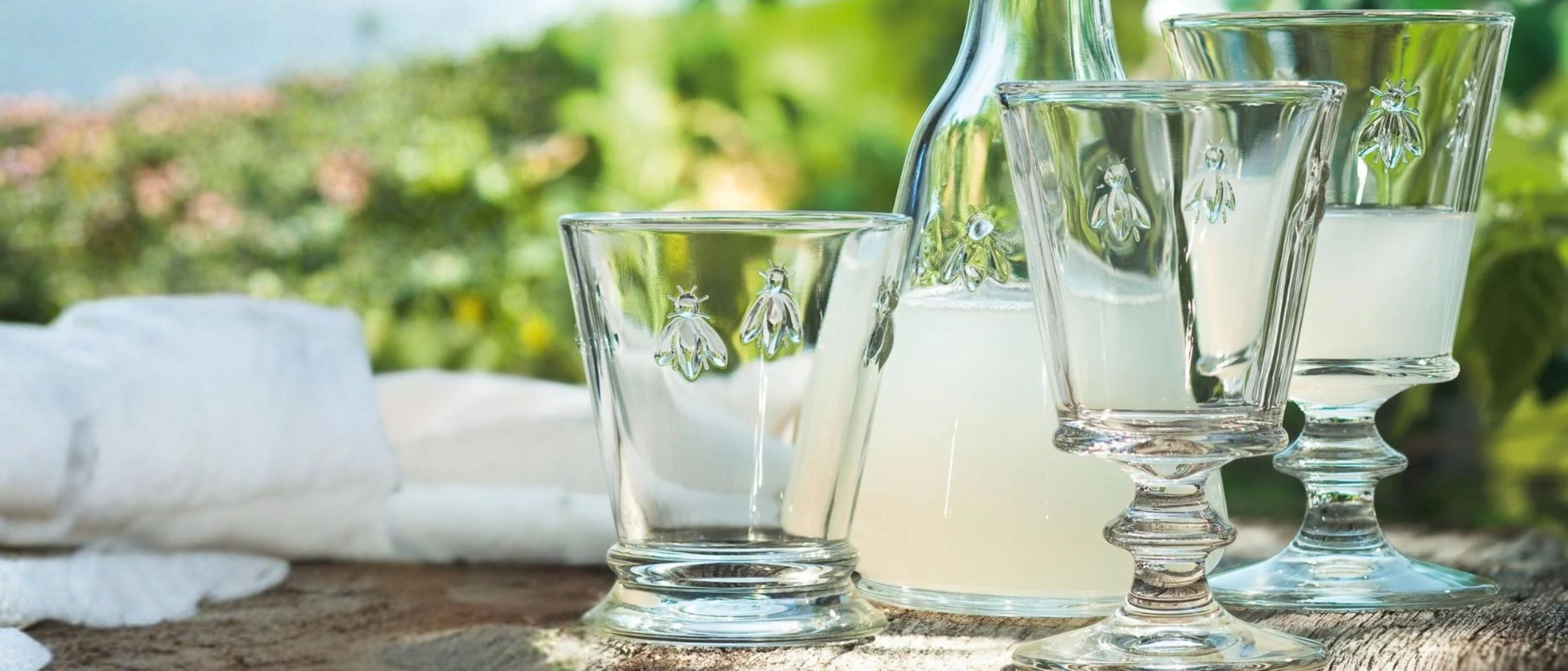Clear glassware with drinking glasses and a carafe styled outdoors on a wooden table.