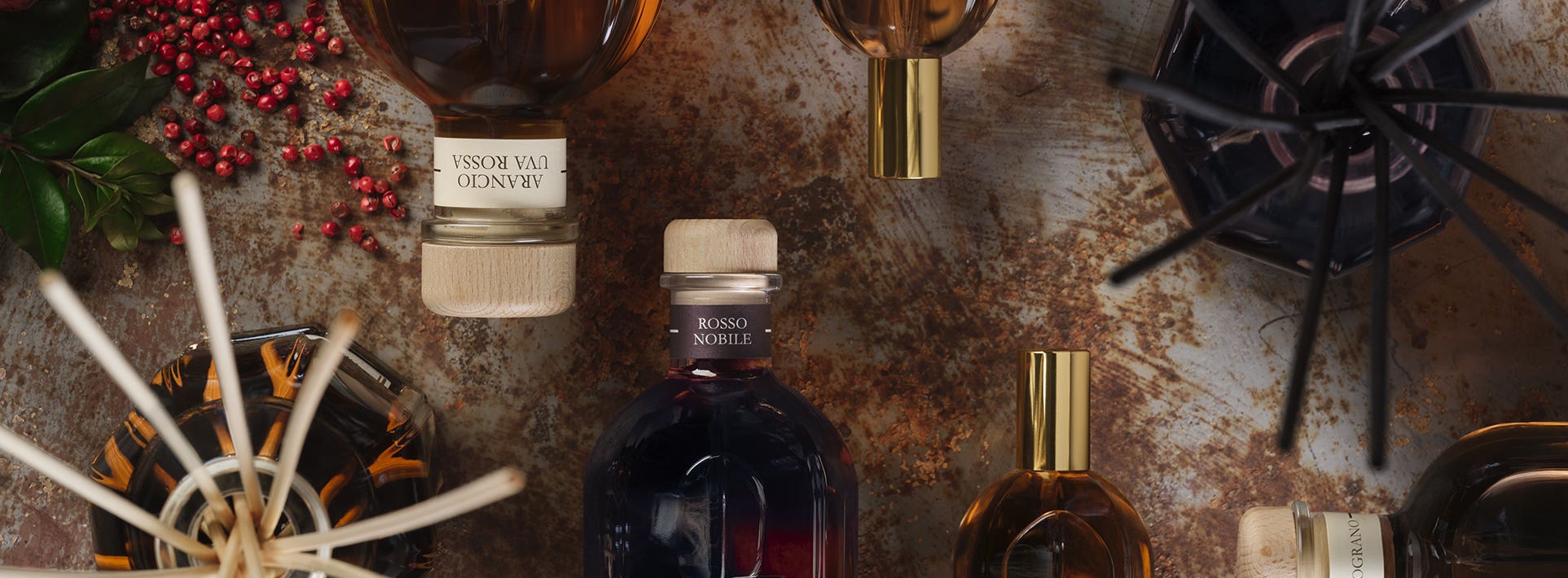 Home fragrance collection with diffusers, diffuser refills, scented candles, and red berries on a textured surface.