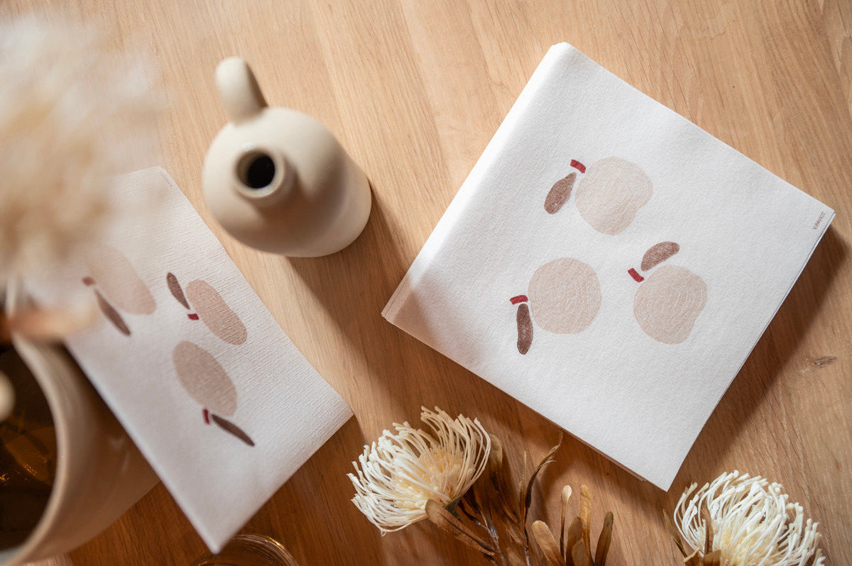 Patterned linen napkins displayed on a wooden table with a decorative vase.