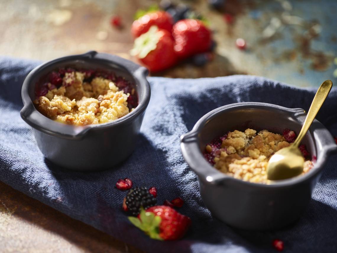 Ramekins and soufflé dishes with baked desserts, crumb topping, and a gold spoon on dark linen.