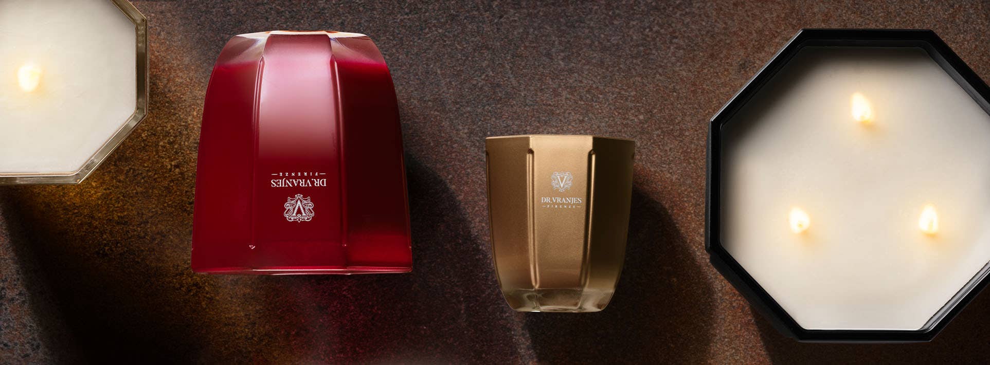 Luxury scented candles in red, amber, and black glass vessels on a dark surface.