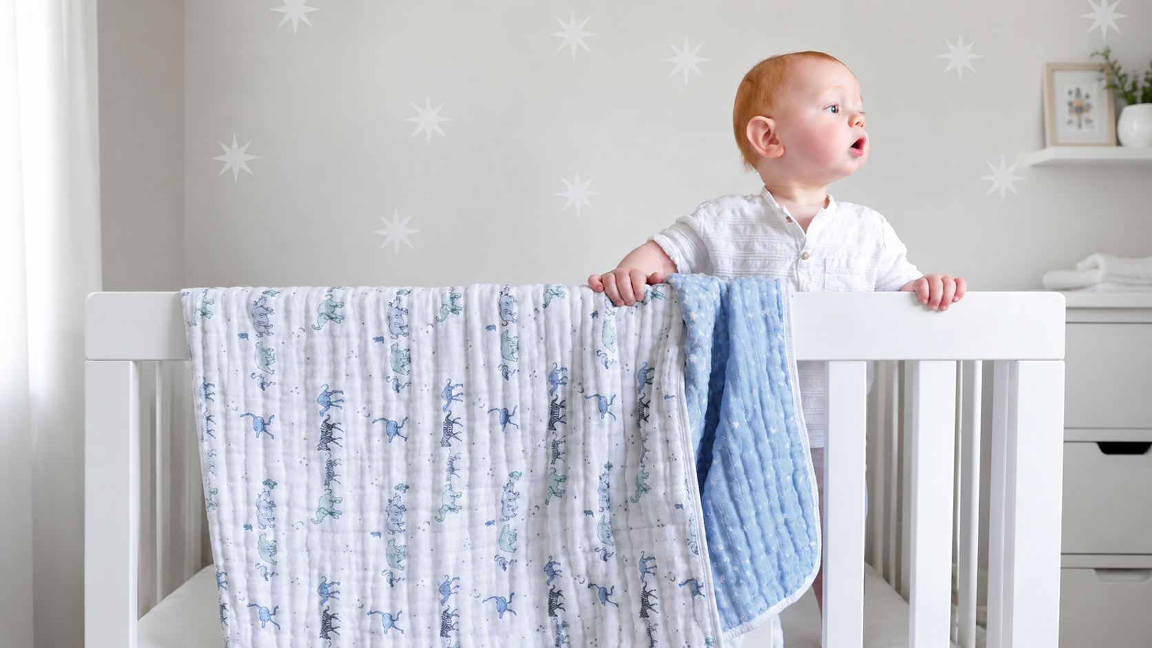 Baby standing in a crib with patterned swaddles and blankets draped over the rail.