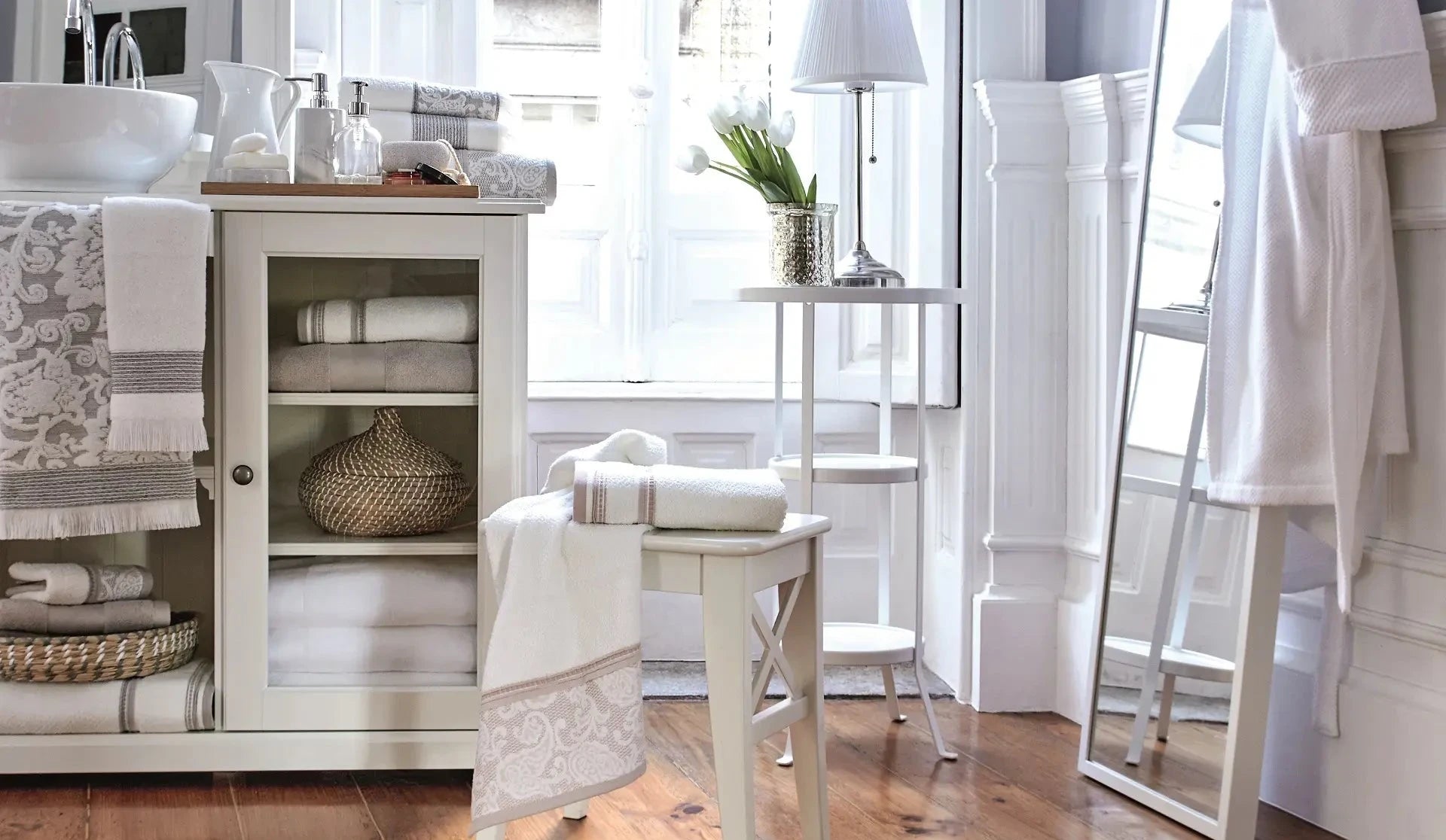 Bathroom towel collection with folded and hanging towels, cabinet storage, flowers, and bath accessories.